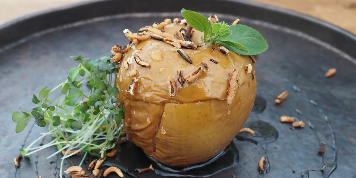 A smoked apple served on a black plate with herbs and seeds