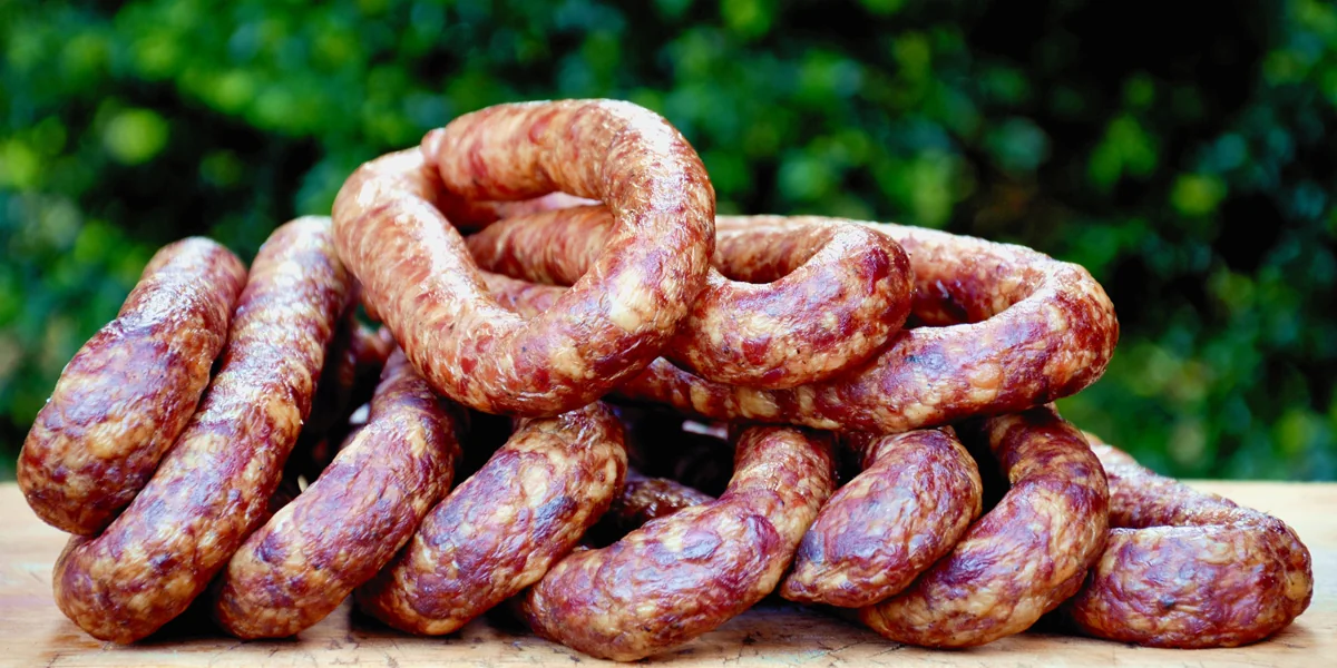 Smoked sausages stacked on a wooden board outdoors